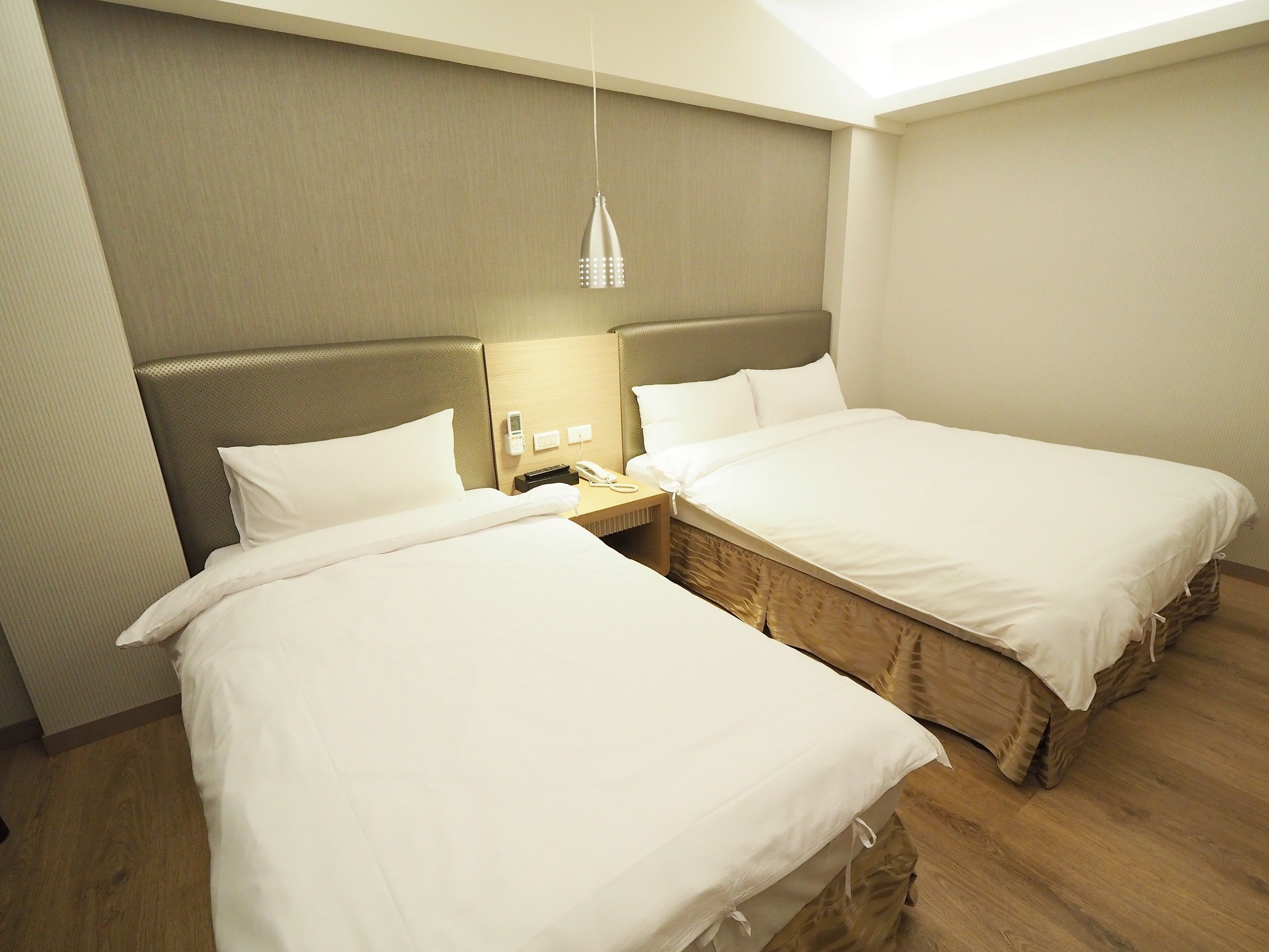 A hotel room with two single beds, a bedside table with a lamp, a phone, and a small nightstand.