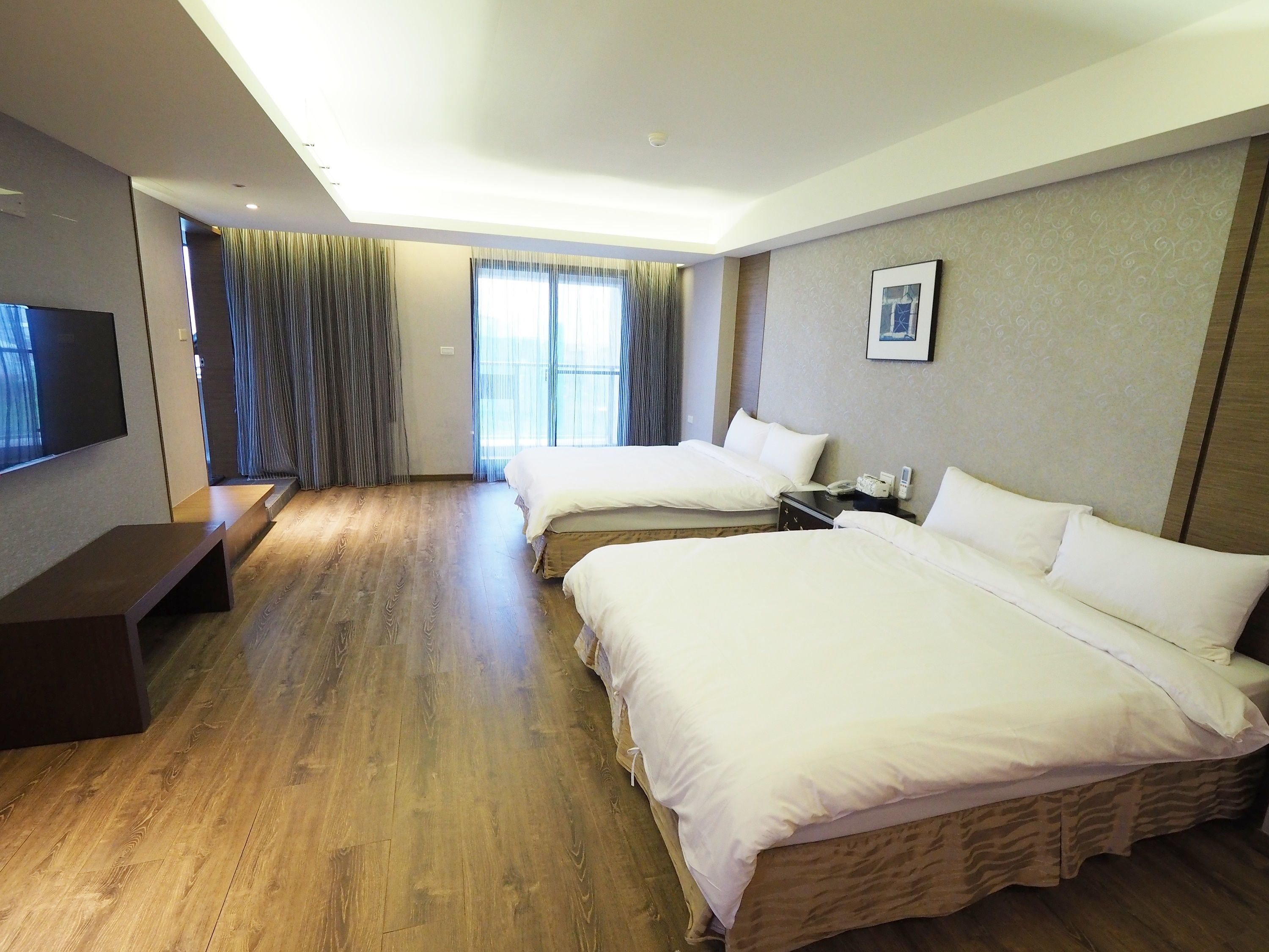 Quarto de hotel com duas camas, uma televisão de tela plana, mesa de cabeceira e janela com cortinas.