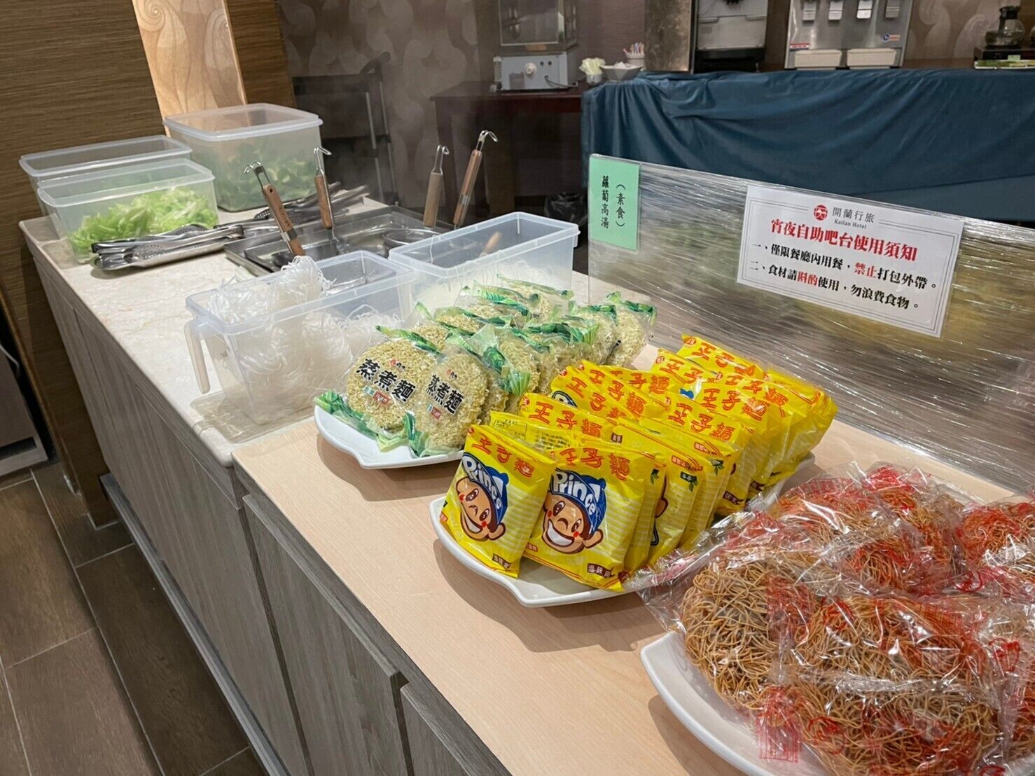 A buffet counter with various food items including packaged noodles, rice cakes, and other snacks.