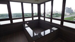 A modern bathroom with a large bathtub, dark tiles, and large windows offering a city view. - Kailan Hotel (Toucheng)