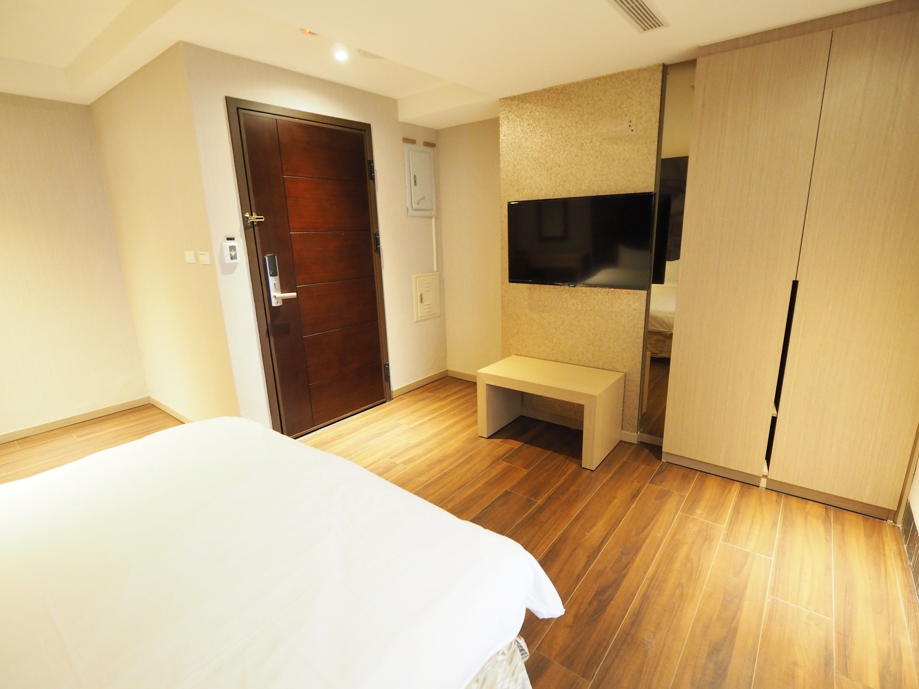 A bedroom with a bed, a wooden floor, a wardrobe, and a bench.