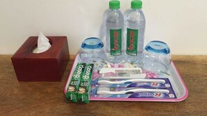 Una bandeja con artículos de tocador personal, incluyendo una caja de pañuelos, dos botellas de agua, un cepillo de dientes y pasta dental.