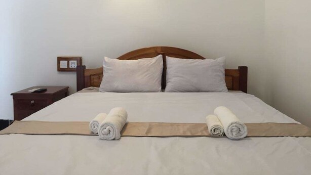 Una cama bien tendida con sábanas blancas y dos toallas enrolladas al pie.