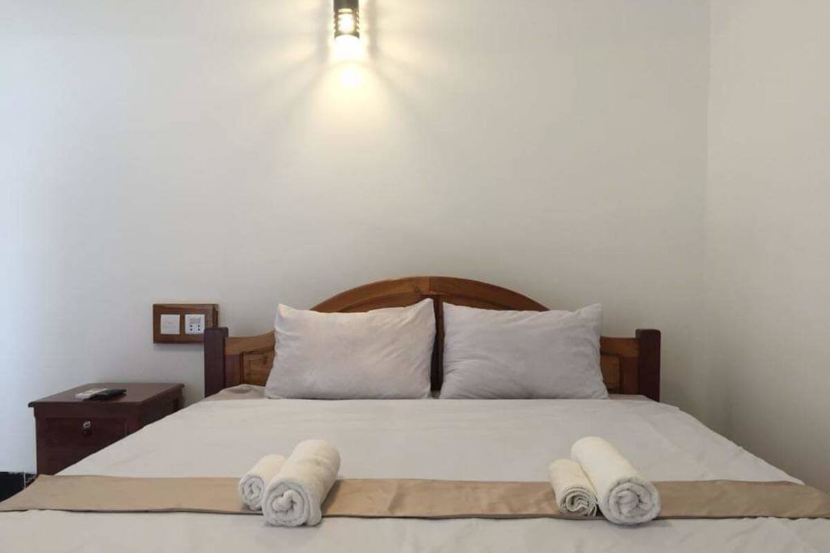 A neatly made bed with white linens and two rolled towels placed at the foot of the bed.