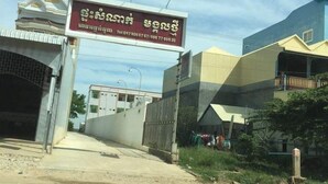 Entrada de un edificio con un letrero en un idioma extranjero, un área amurallada y una calle con pasos para peatones.