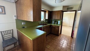 Een compacte keuken met houten kastjes, een groen aanrechtblad, een inbouwgootsteen en een betegelde vloer.