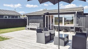 Une terrasse avec des meubles d’extérieur, un espace couvert équipé d’un téléviseur et, au fond, une clôture en bois.