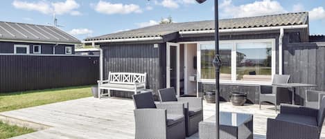 A deck with outdoor furniture, a covered area with a TV, and a wooden fence in the background.