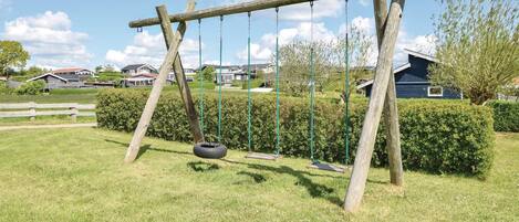 A wooden swing set with a tire swing, surrounded by a well-maintained lawn and hedges, with houses in the background.