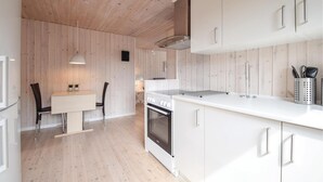 Une cuisine moderne avec des murs recouverts de panneaux en bois, des meubles blancs, un îlot central et un coin repas comprenant une table et des chaises.