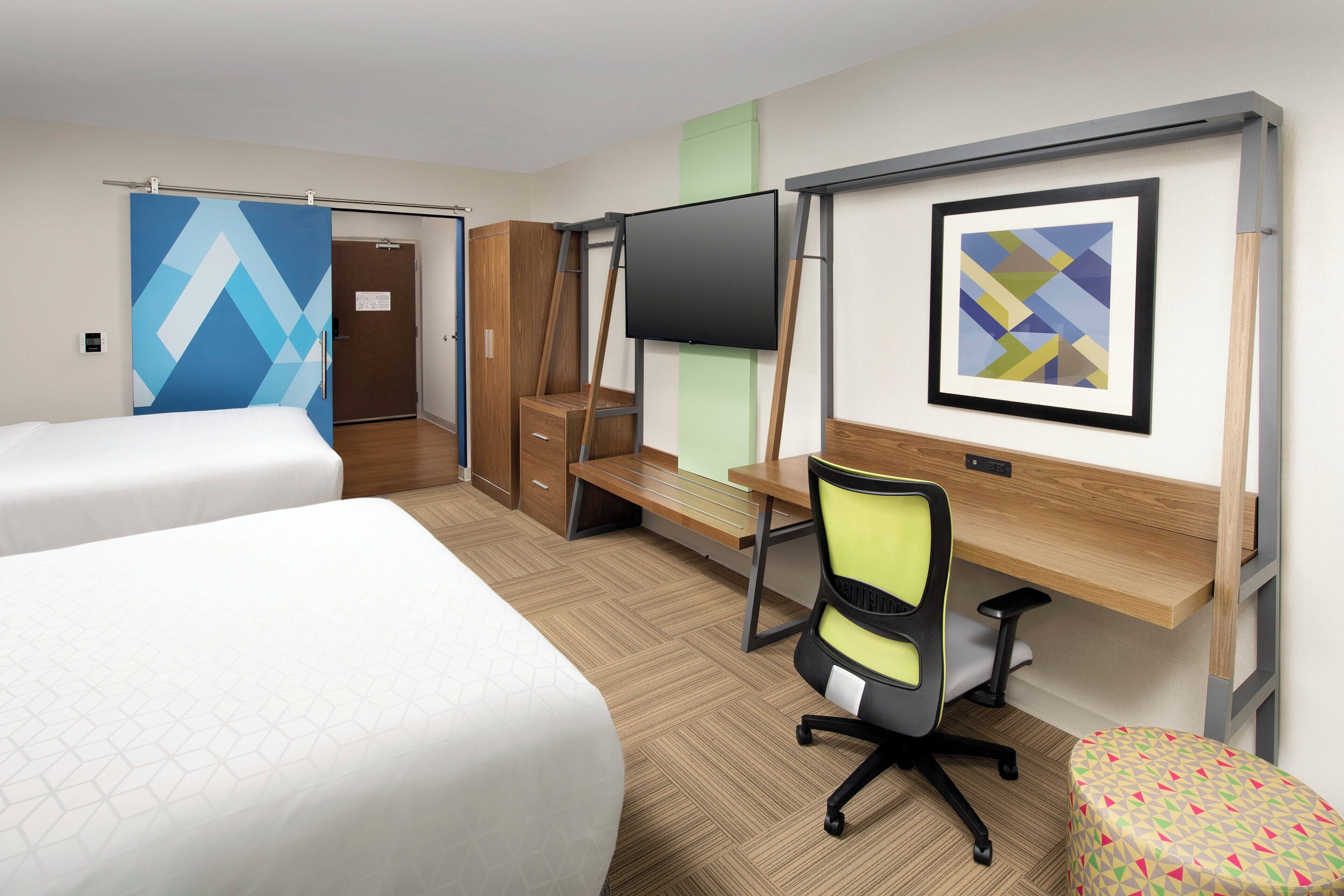 A hotel room with two beds, a desk with a chair, a flat-screen TV, and a framed picture on the wall.