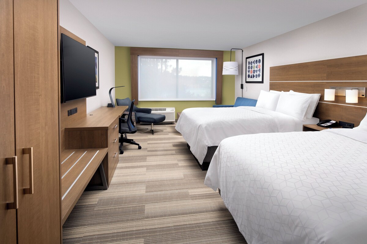 A hotel room with two beds, a desk, a chair, a television, and a window with a view.