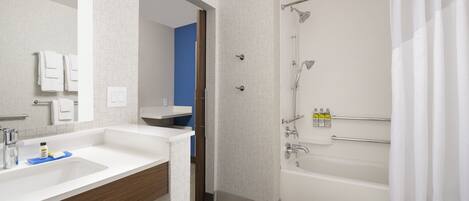 Un baño moderno con lavamanos, espejo y bañera blancos. Se ve una cortina de ducha y un perchero.