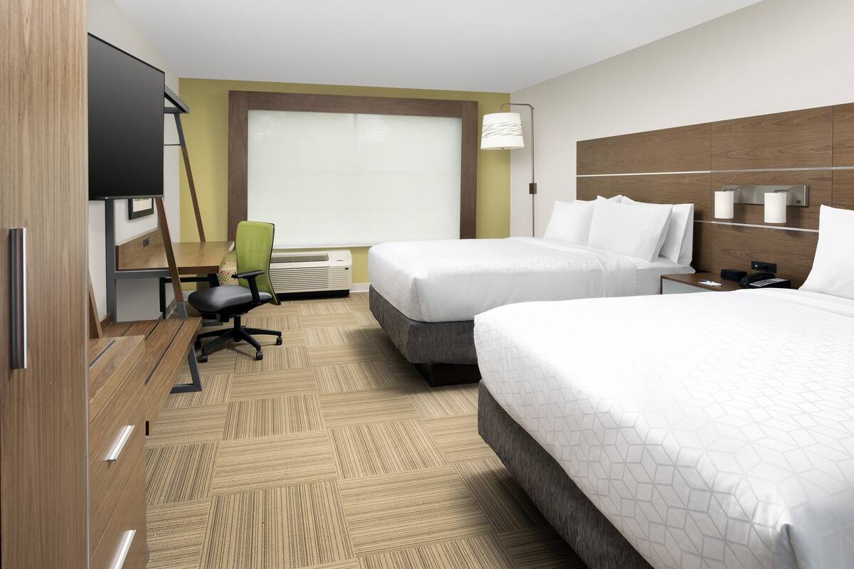A hotel room with two beds, a desk, a chair, a TV, and a window with blinds.