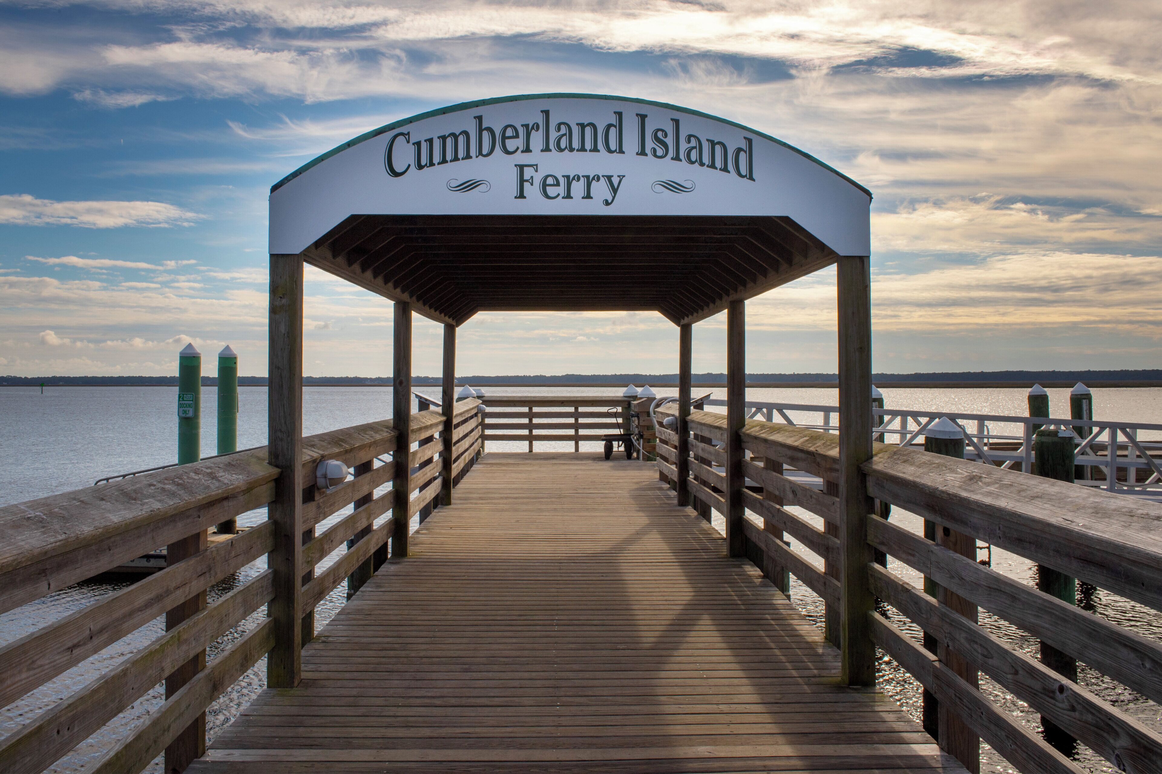 Een houten steiger die leidt naar een overdekt gebied met een bord waarop staat 'Cumberland Island Ferry'.