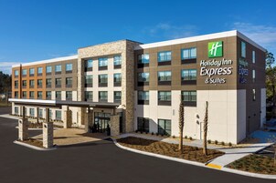 Edificio de Holiday Inn Express con diseño moderno, que cuenta con una entrada cubierta y un área ajardinada con árboles pequeños.