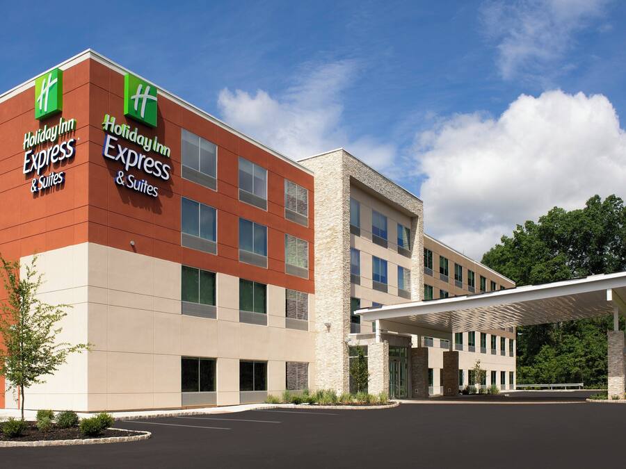 A Holiday Inn Express & Suites hotel with a modern design, featuring a prominent green and white logo, a covered entrance, and a parking lot.
