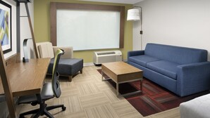 Ein modernes Hotelzimmer mit Schreibtisch aus Holz, einem blauen Sofa, einem kleinen Couchtisch und einem Fenster mit Jalousien.