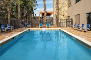 Piscina com superfície de água límpida, cercada por grade e equipada com espreguiçadeiras azuis.