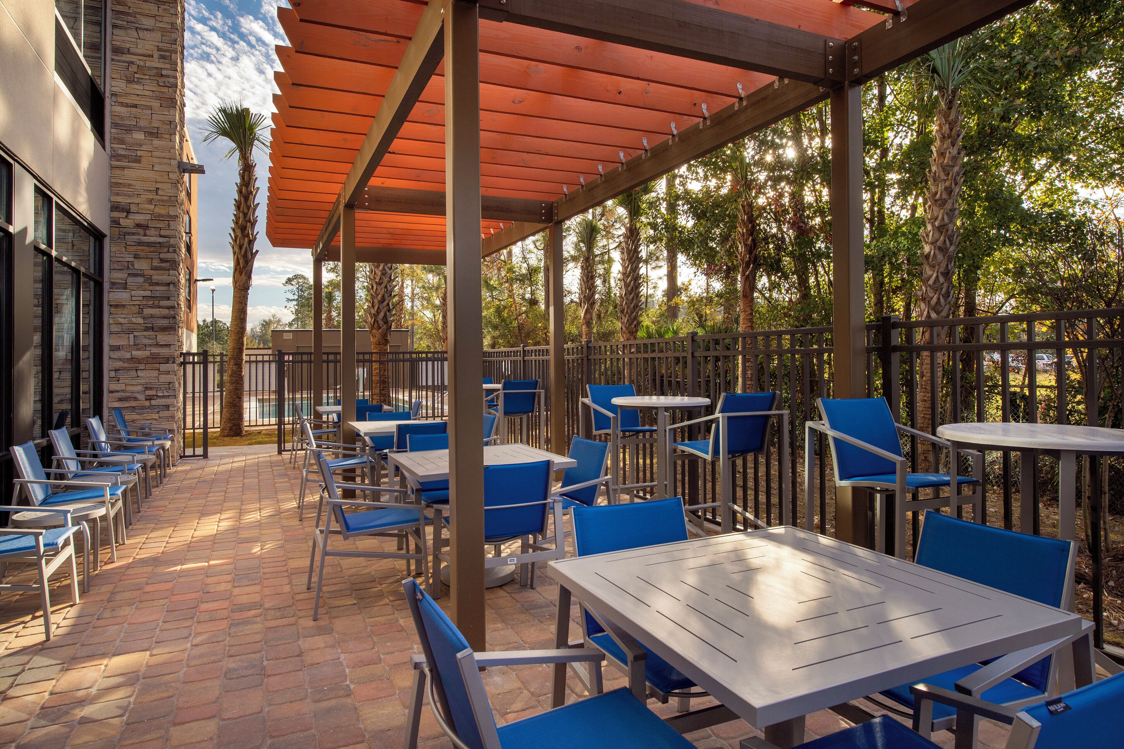 An outdoor patio with tables and chairs, a stone building, and a wooden pergola.