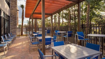 An outdoor patio with tables and chairs, a stone building, and a wooden pergola.