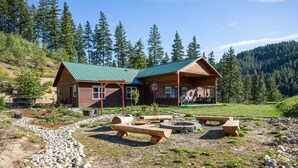 A cabin with a green roof, wooden exterior, and a deck area with picnic tables and fire pits. - Spacious Private Lodge with Mountain Views (Leavenworth)