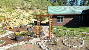 A garden with a wooden pergola, potted plants, and a wooden cabin with a green roof. - Spacious Private Lodge with Mountain Views (Leavenworth)