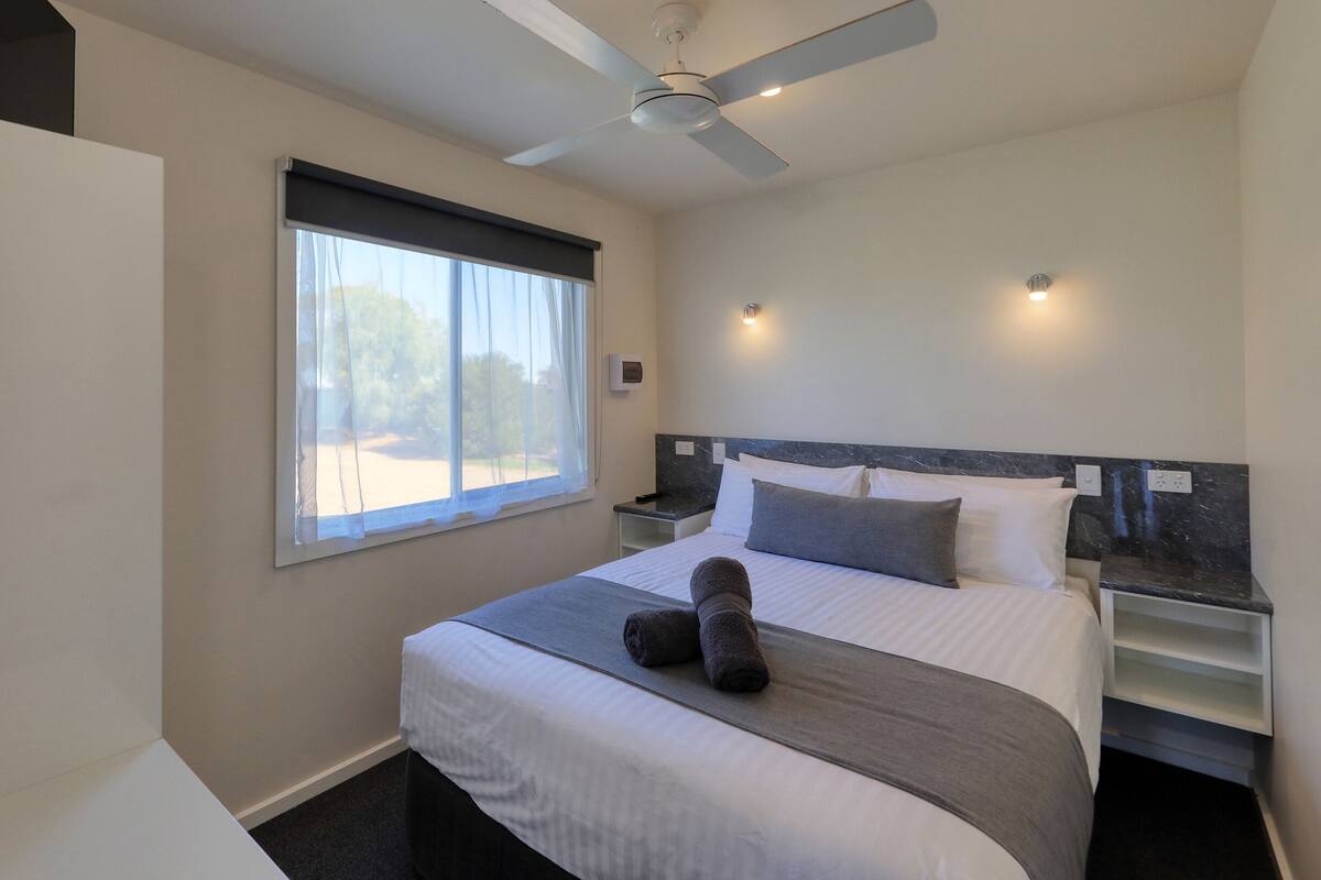 A modern hotel room with a large bed, a ceiling fan, a window with sheer curtains, and a marble headboard.