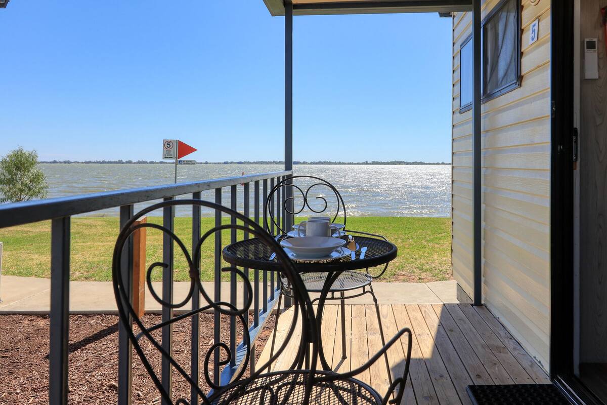A covered outdoor area with a table and chairs, overlooking a body of water.