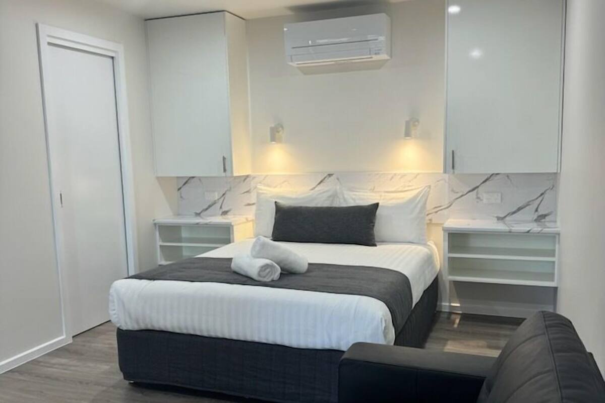 A modern bedroom with a bed, bedside tables, a ceiling fan, and built-in shelving.