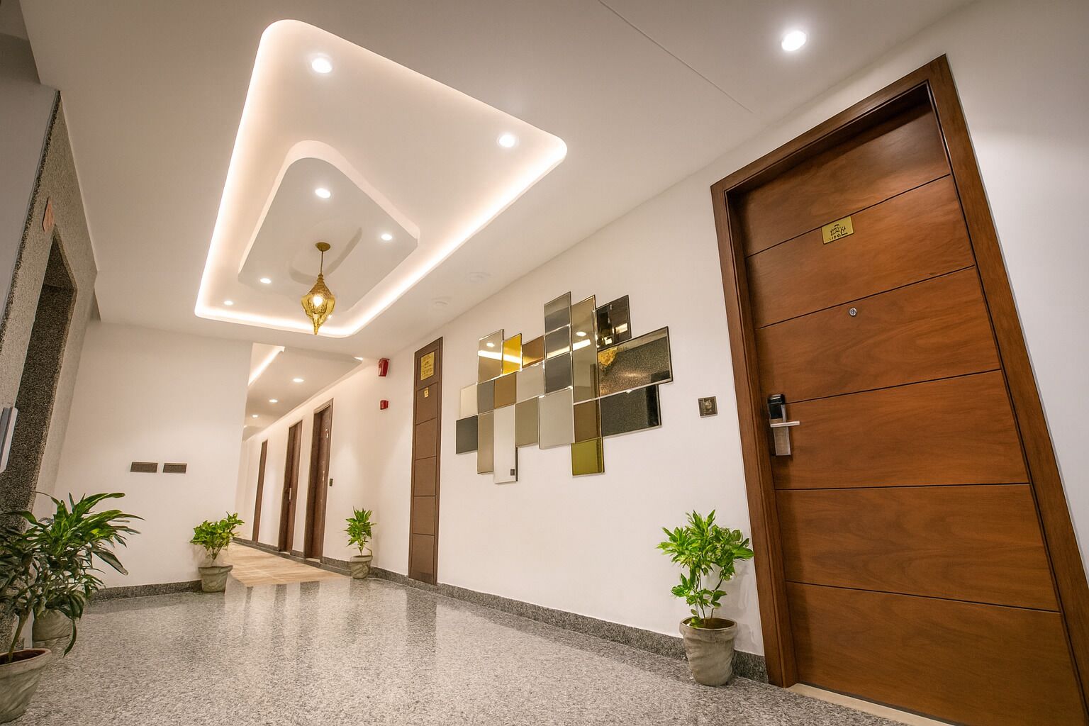A modern hotel lobby with a polished granite floor, wooden doors, and a decorative ceiling light fixture.