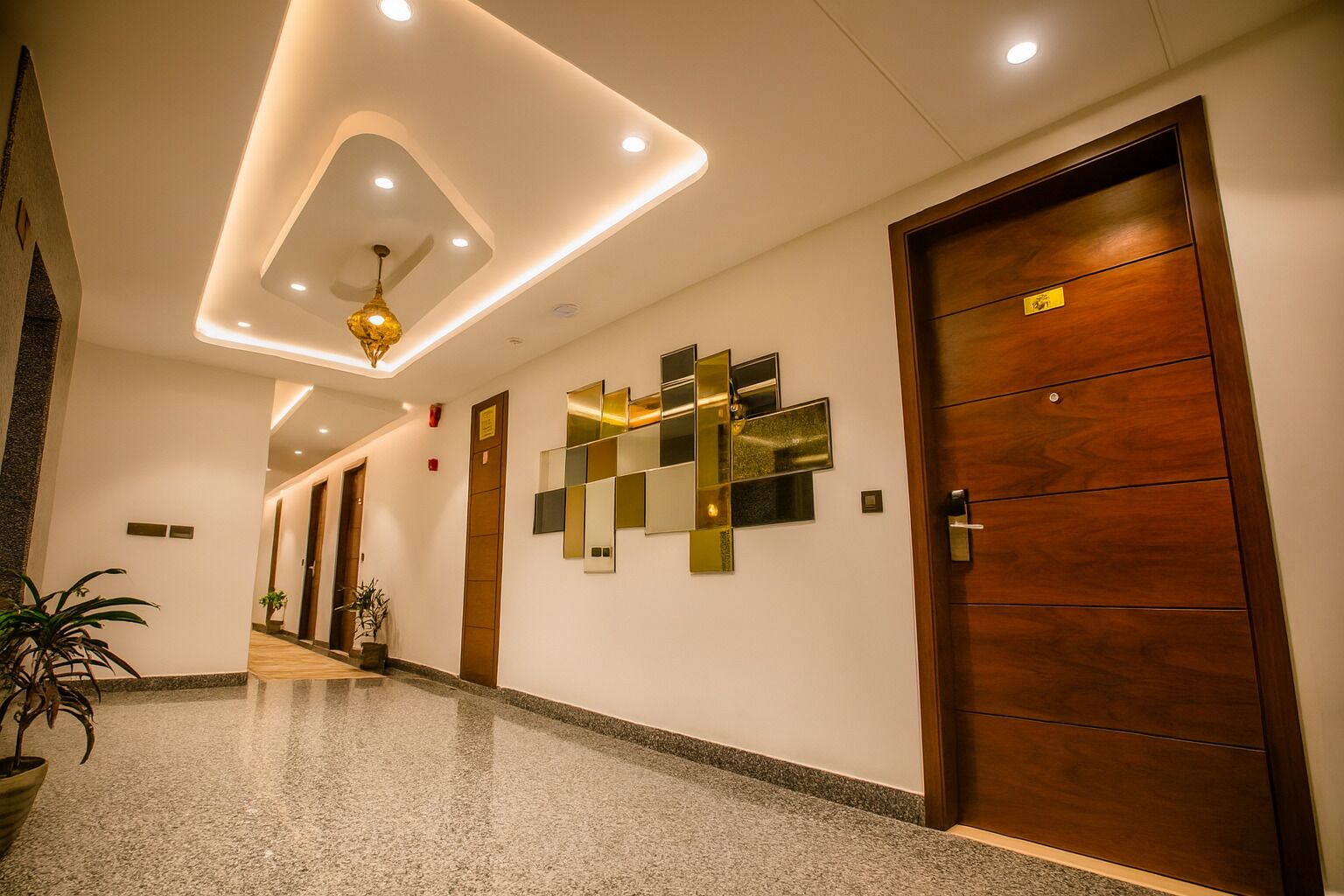 A modern hotel lobby with a polished granite floor, a geometric wall art installation, and a wooden door with a sign.