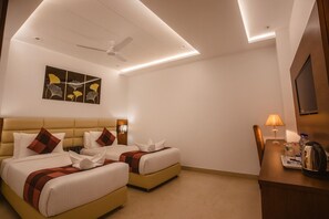 Ein Hotelzimmer mit zwei Betten, einem Schreibtisch, einem Sessel, einem Deckenventilator und einem an der Wand befestigten Fernseher.