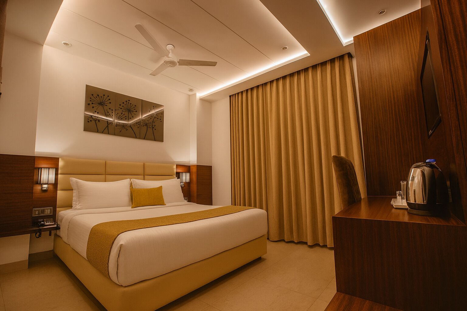 A hotel room with a large bed, a desk with a kettle, a ceiling fan, and a painting on the wall.