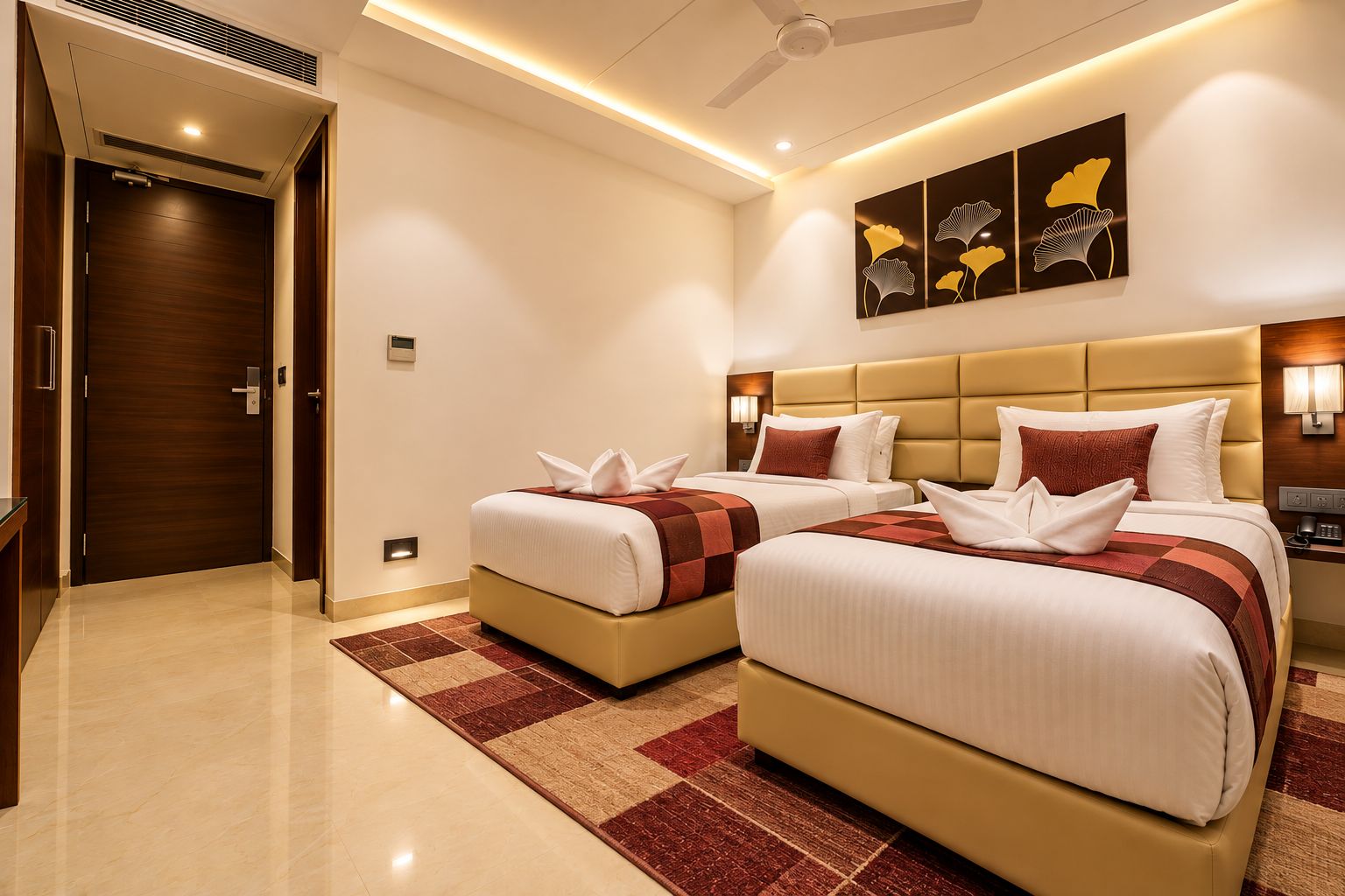 Habitación de hotel con dos camas, una puerta de madera, un ventilador de techo y cuadros en la pared.