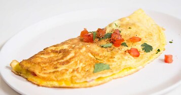 Omelete em prato branco com tomate picado e ervas.