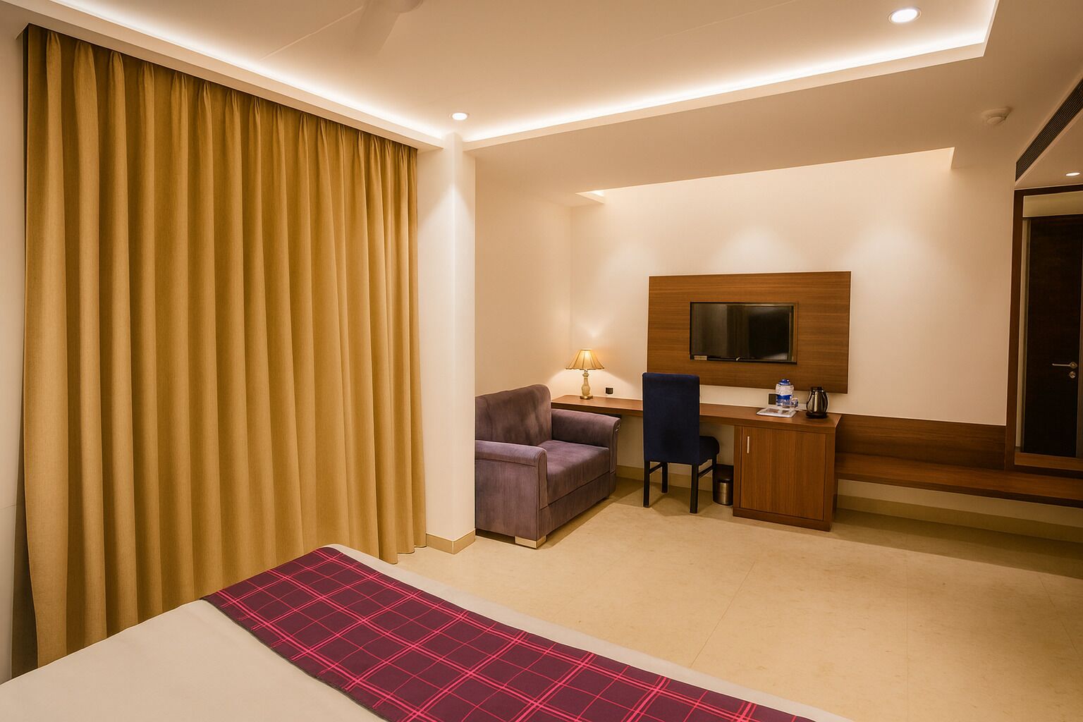 A hotel room with a bed, a desk, a chair, a TV, and a large window with curtains.