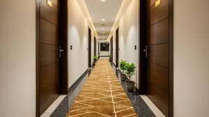 A hotel hallway with wooden doors, a patterned carpet, and potted plants. - HOTEL TEN SQUARE - 5 Minutes from The Taj Mahal (Agra)