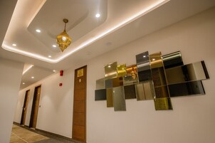 Un pasillo moderno de hotel con una lámpara decorativa en el techo, un espejo en la pared y una puerta de madera con un letrero.