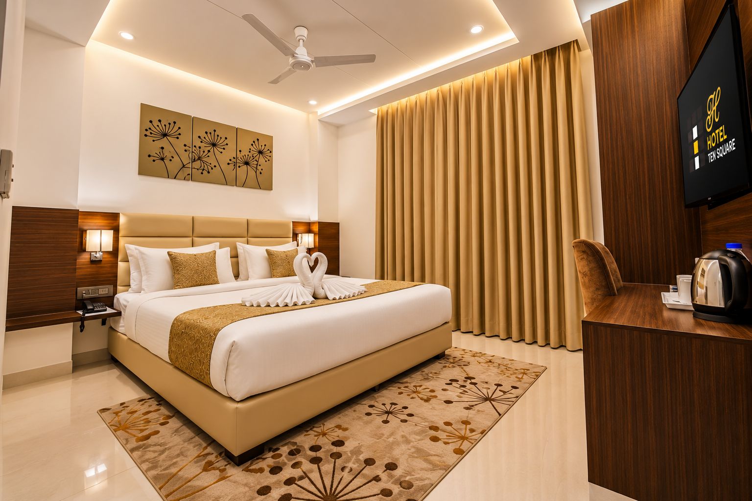 Une chambre d’hôtel avec un grand lit, un bureau avec une bouilloire, une télévision à écran plat et un ventilateur de plafond.