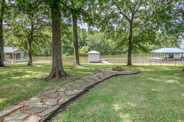 A stone pathway leading to a gazebo, surrounded by lush greenery and a small dock by a calm lake.