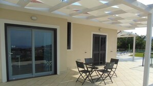 Une terrasse extérieure avec une table et des chaises, une porte vitrée donnant sur un balcon et un espace couvert offrant une vue sur la ville.