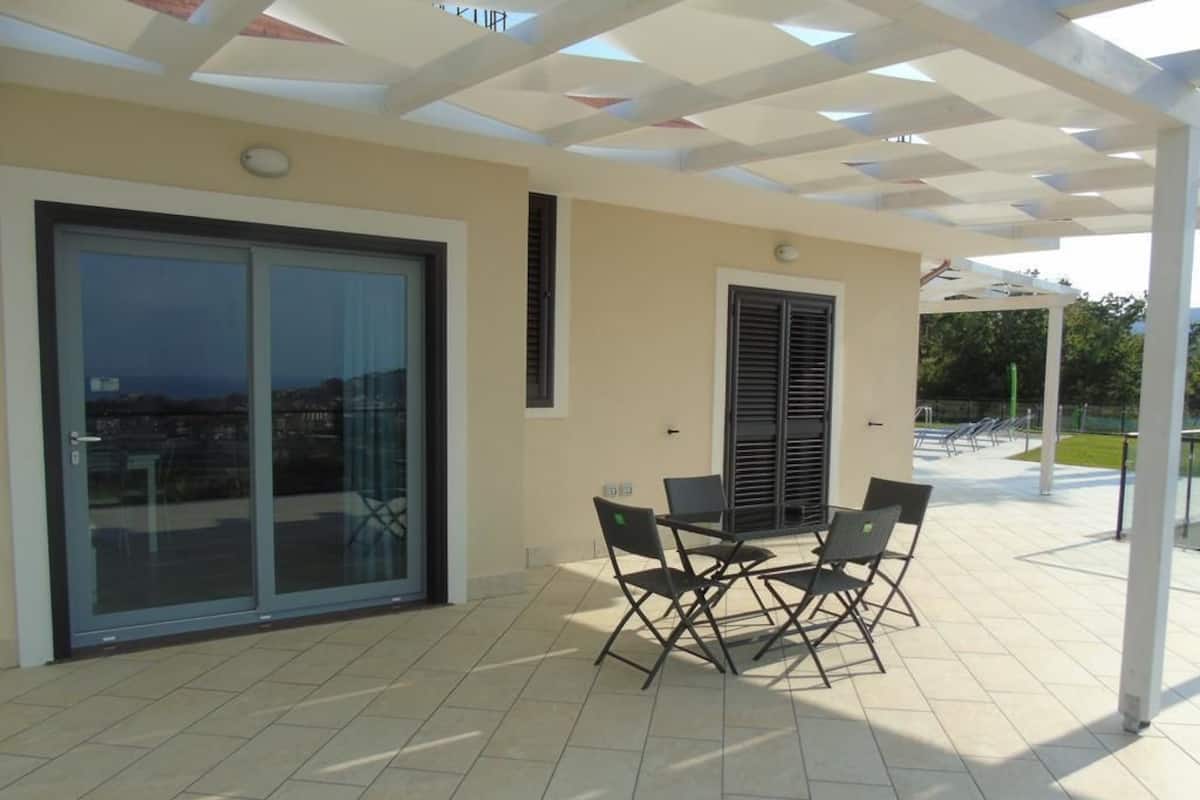 Une terrasse extérieure avec une table et des chaises, une porte vitrée donnant sur un balcon et un espace couvert offrant une vue sur la ville.