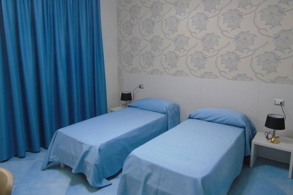 Une chambre avec deux lits simples, un papier peint à motifs, un rideau bleu et des lampes de chevet.
