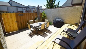 A patio with a table and chairs, a trash can, and a wooden fence.