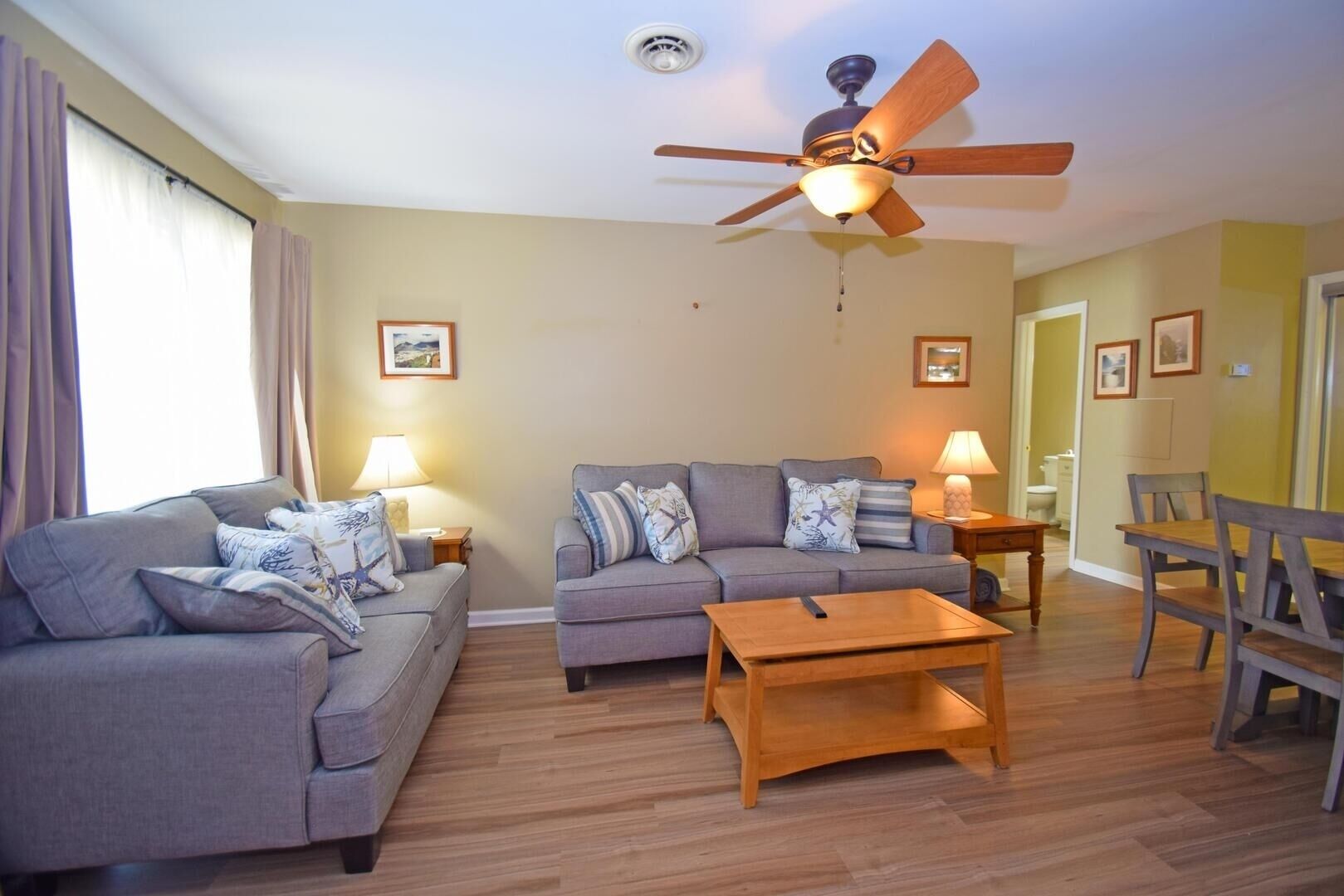 A living room with two sofas, a coffee table, a ceiling fan, and a dining area with a table and chairs.