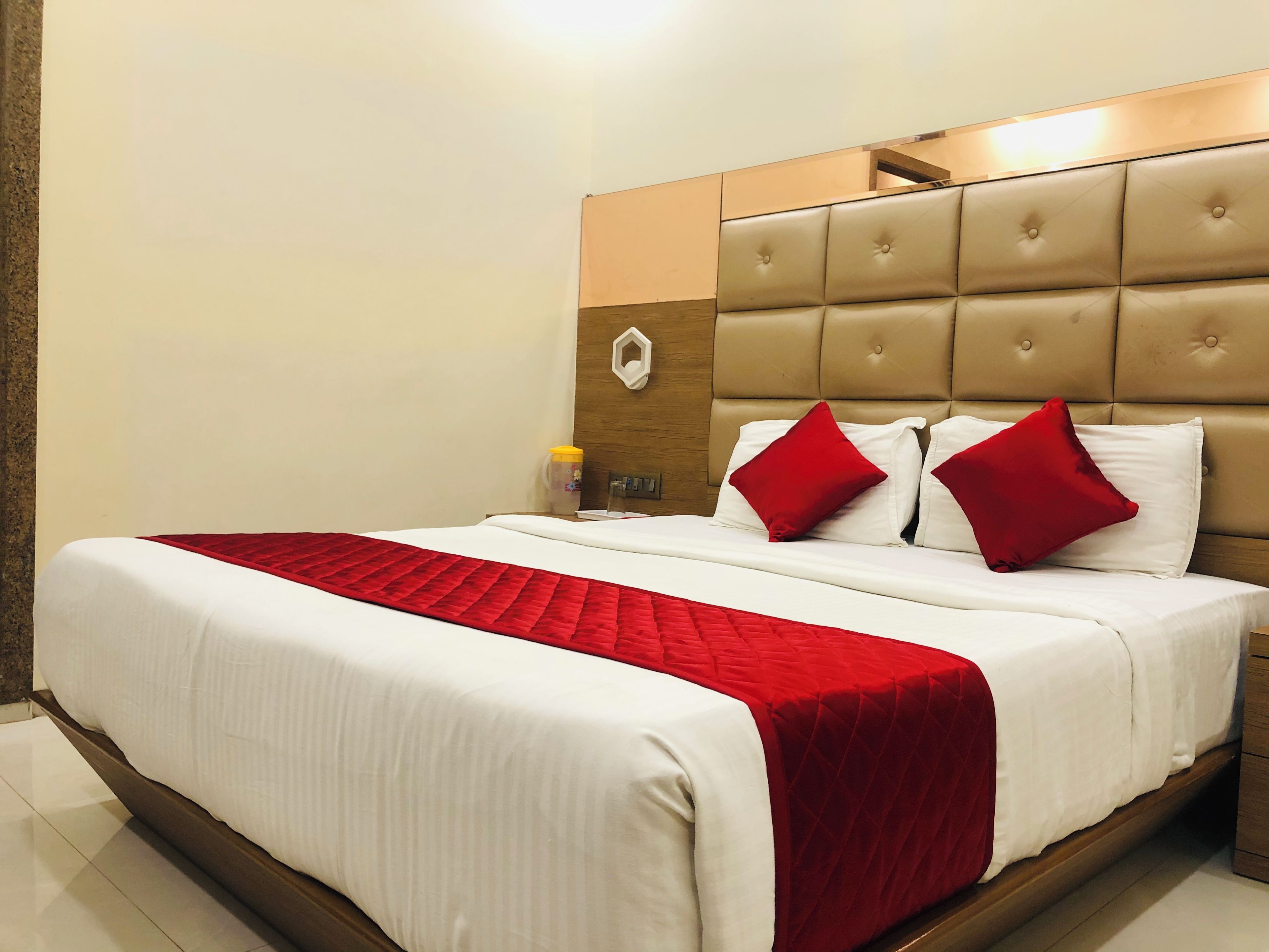 A hotel room with a large bed, a wooden headboard, and a red throw blanket.