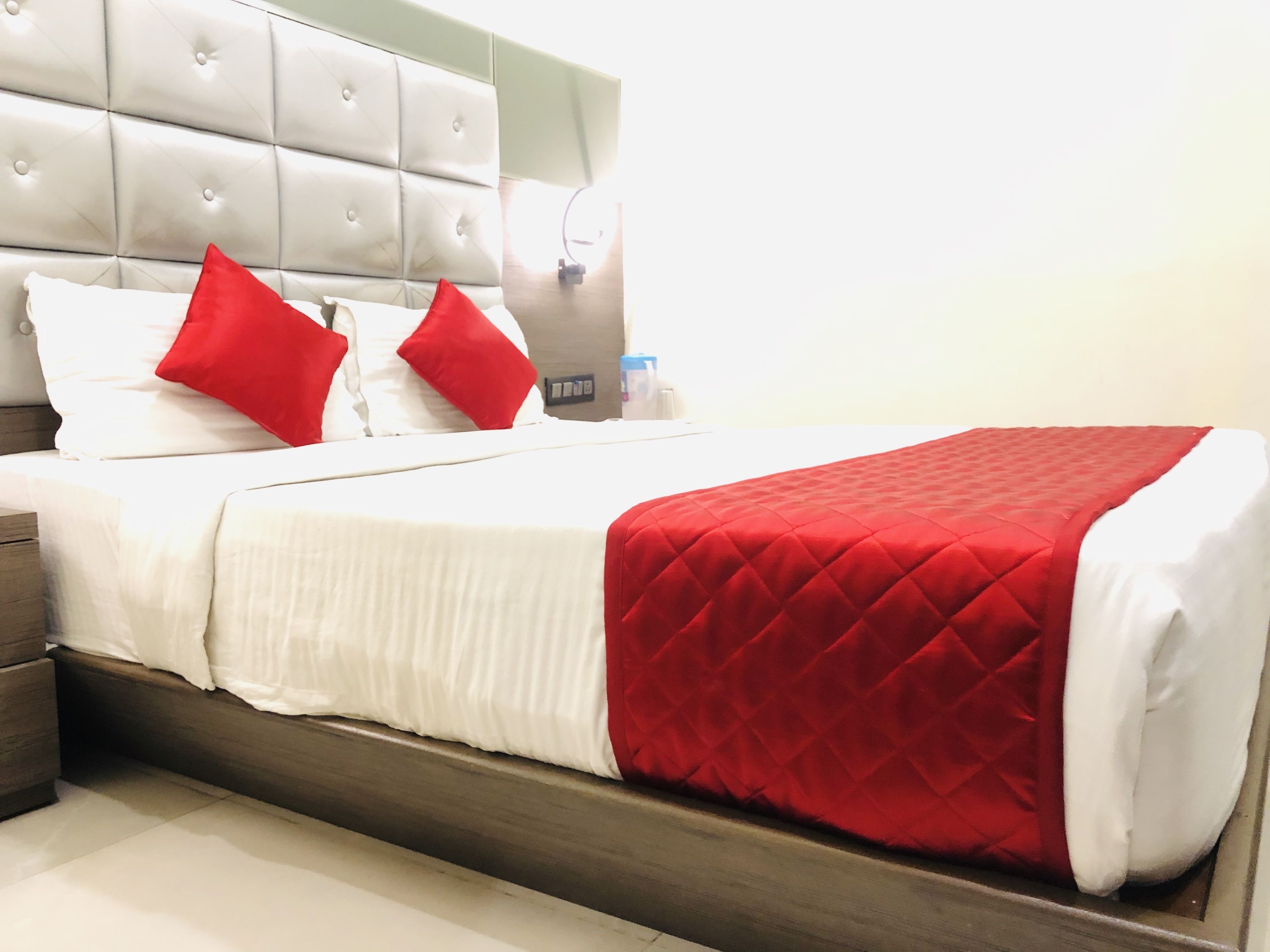 Een hotelkamer met een gestapeld hoofdbord, een bed met wit en rode beddengoed, en een rode gebogen plaid.