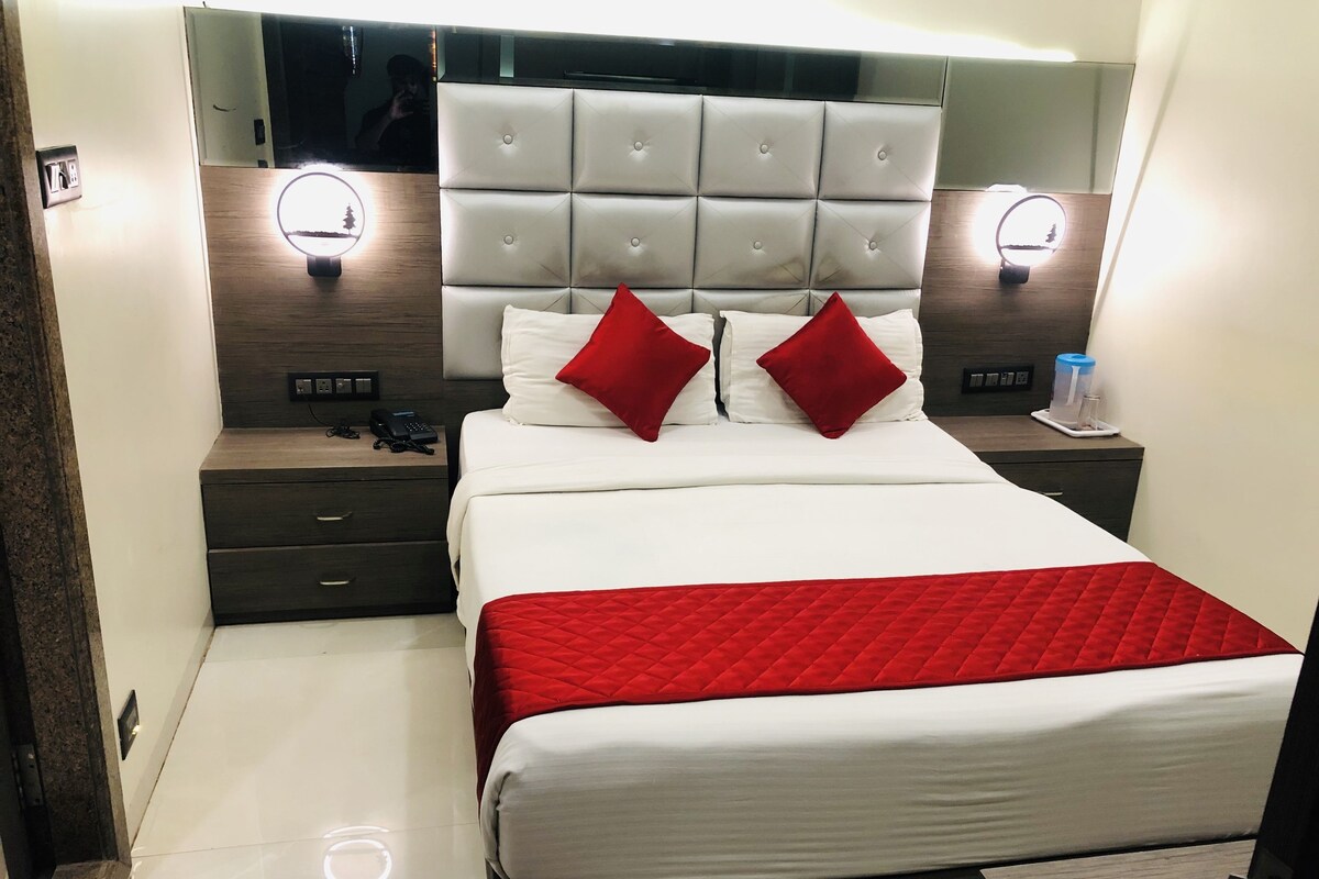 A modern hotel room with a large bed, two bedside tables, a nightstand, and a headboard with built-in lighting.
