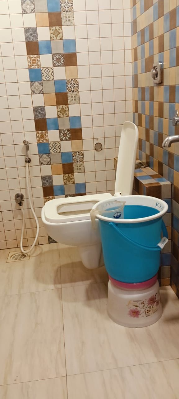 A bathroom with a toilet, a shower, and a blue bucket.